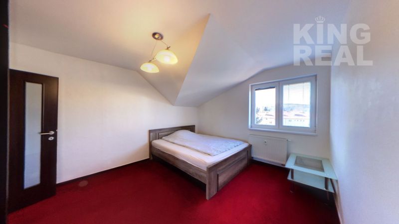 Bedroom in a two-room apartment with a simple bed and a red carpet.