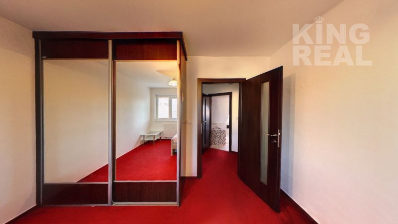 Interior of a 2-room apartment with a red carpet and a built-in wardrobe with a mirror.