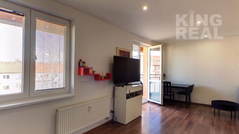 Living room in a two-room apartment with a television and wooden decor flooring.