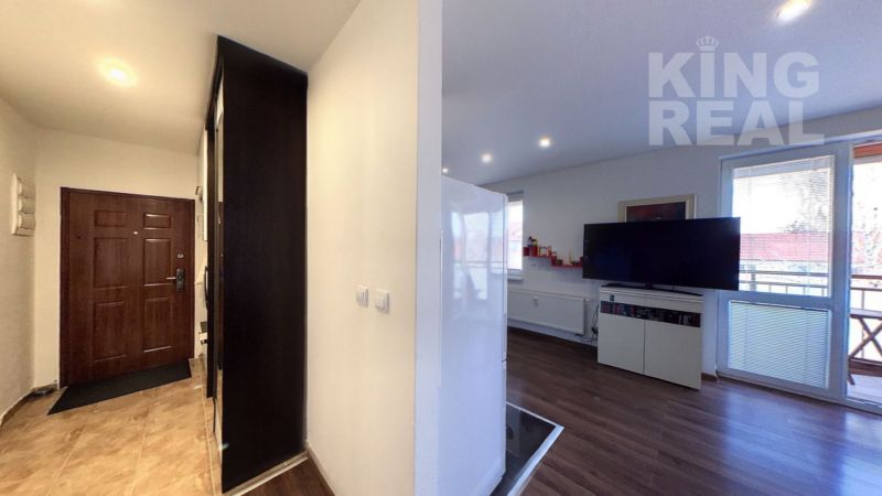 Entrance hall with tiles and living room with wood-patterned flooring in a 2-room apartment.