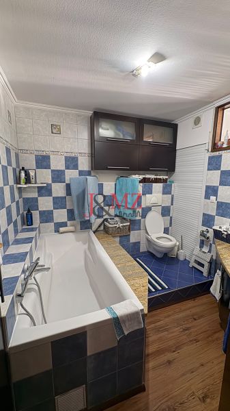 A bathroom with a bathtub, blue tiles, and a wooden decor floor in a 3-room apartment.