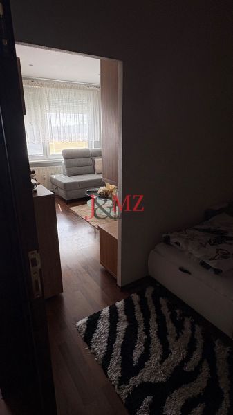 A room in a 3-room apartment with a sofa, a bed, and a floor with a wooden decor.