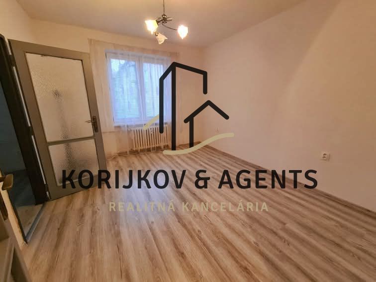 A room in a 2-room apartment with a wooden decor floor and a window with a blind.