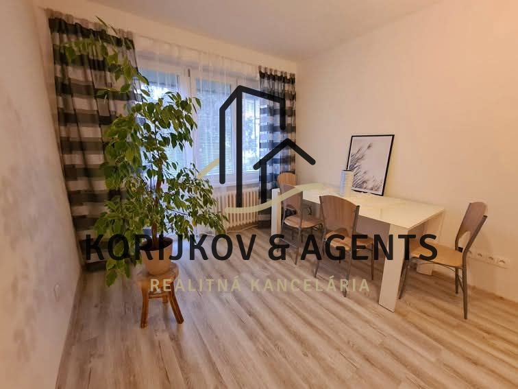 A room in a 2-room apartment with a dining table, chairs, and a floor with a wood decor.
