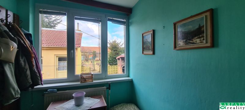 Interior of a family house with coats on a hanger, green walls, and a view from the window.