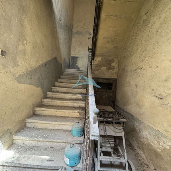 An old staircase in commercial premises with peeling walls and containers on the floor.
