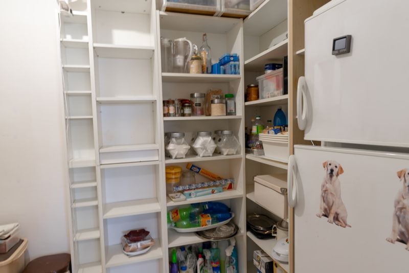 A storage room in a 3-room apartment with shelves full of groceries and a cooling box.
