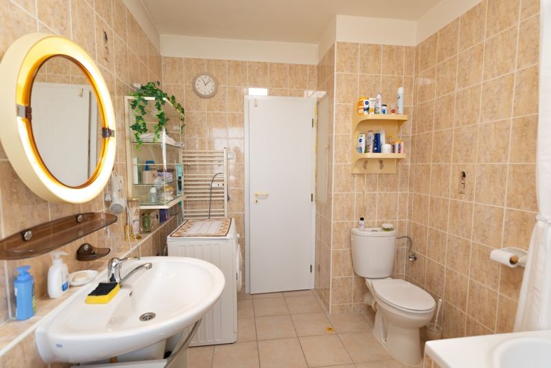 A bathroom in a 3-room apartment with a mirror, shower, and washing machine on a tiled floor.
