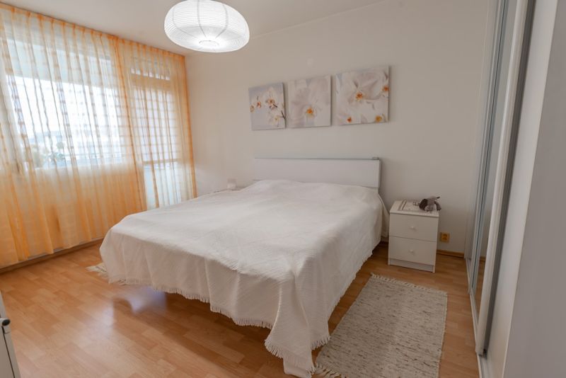 Bright bedroom with a large bed, wood-patterned floor, lamp, and curtains.