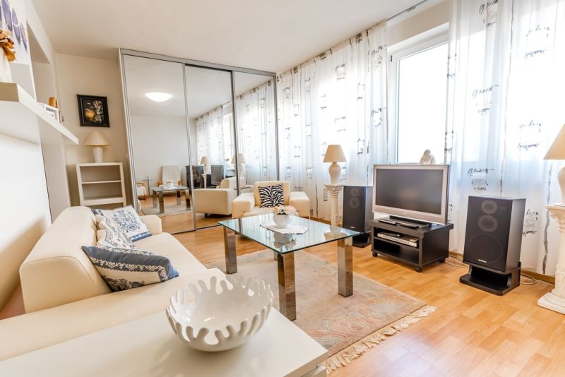 A bright living room with a cream sofa, a glass table, and a wooden decor floor.