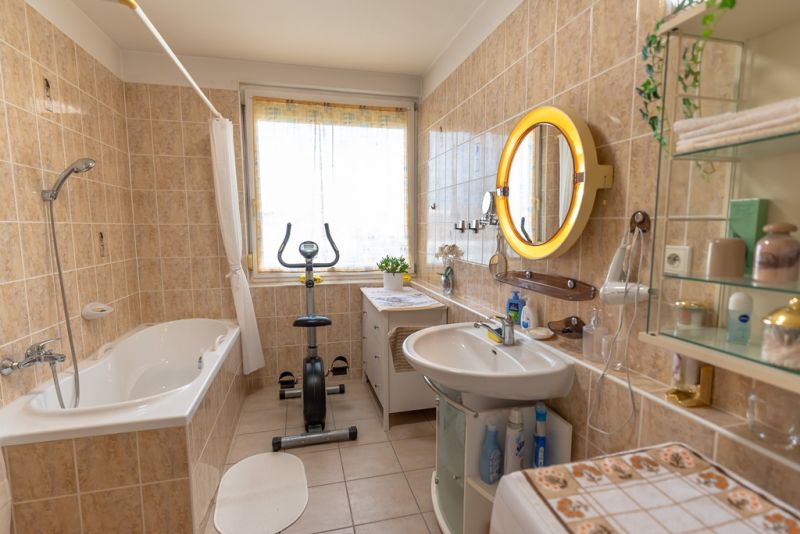 A bathroom with a bathtub, exercise machine, and mirror in a 3-room apartment.