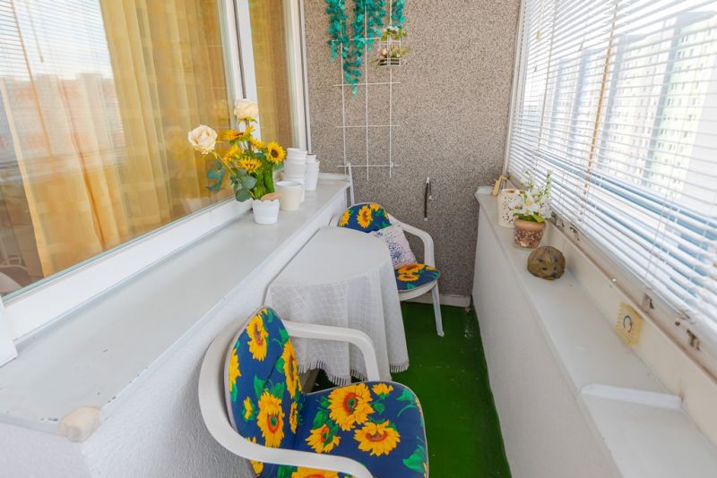 A balcony of a 3-room apartment with chairs and sunflowers, cozily furnished for relaxation.