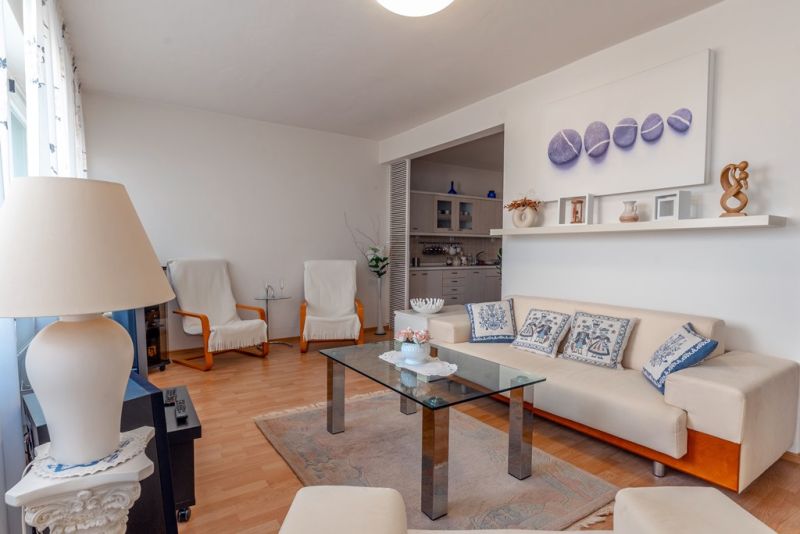 Living room with a sofa, glass table, and wooden decor flooring in a three-room apartment.