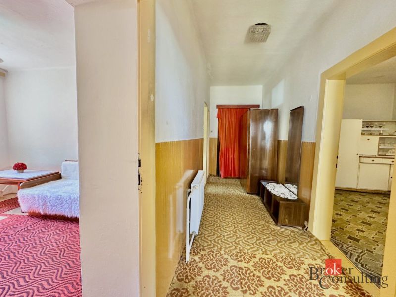 A hallway in a family house with carpets and retro furniture. On the left, a bedroom with red motifs.