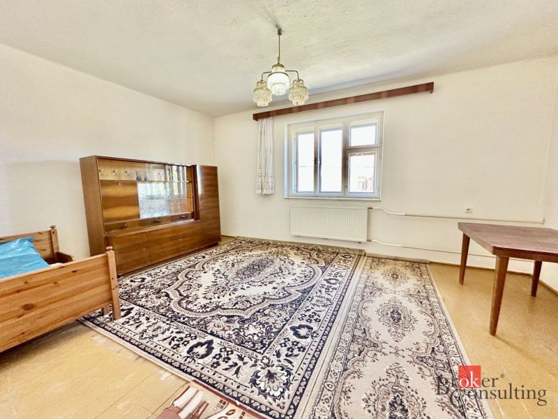 A room in a family house with a carpet, a chair, a wardrobe, and a bed.