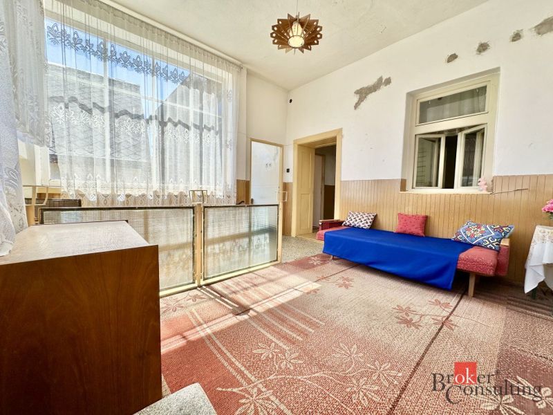 Interior of a family house with a sofa, carpet, and a large window with lace curtains.