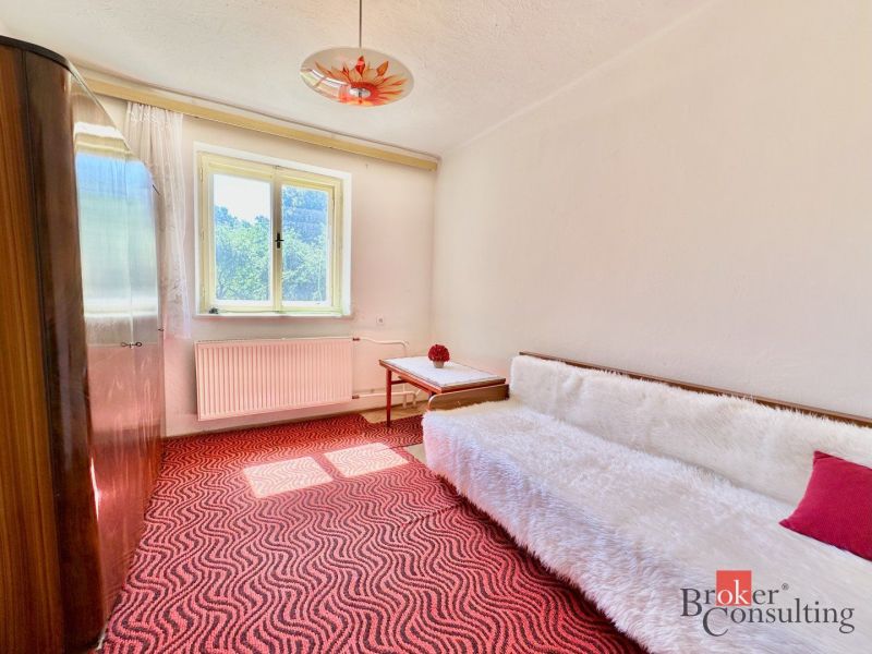A room in a family house with a red carpet, a sofa, and a wardrobe.