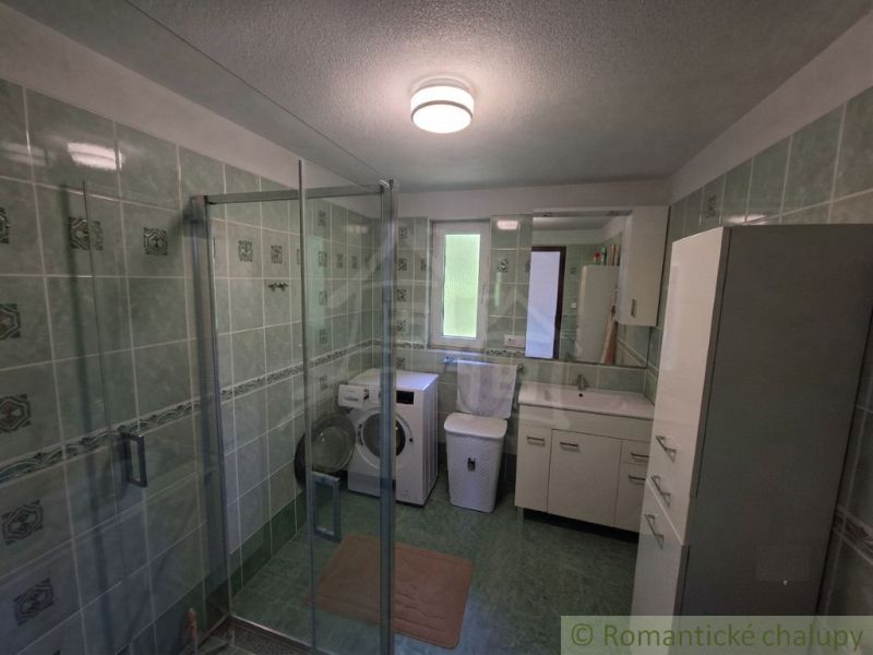 Bathroom in a family house with a washing machine, shower cabin, and green tiles.