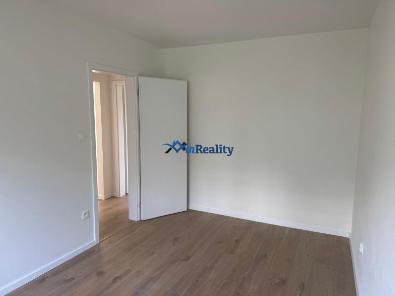 An empty room with white walls and a wood-patterned floor in a three-room apartment.