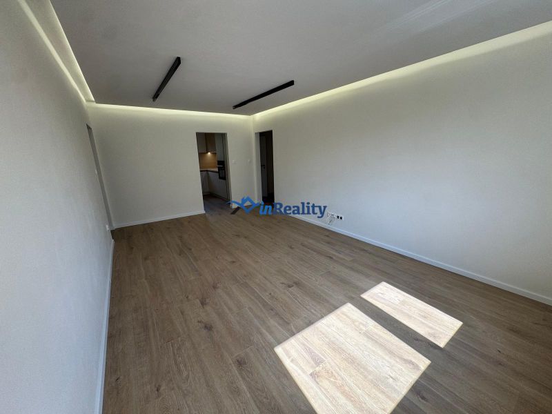 Living room with wood-patterned flooring in a 3-room apartment, light walls, ceiling lighting.