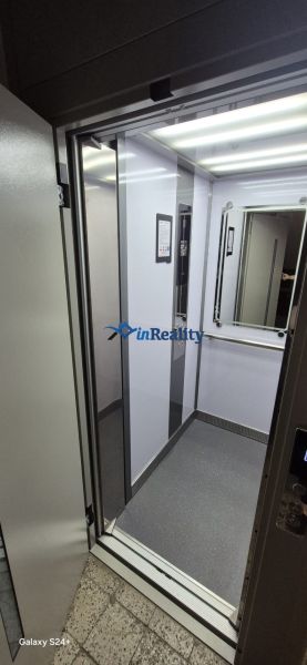 The interior of the elevator in a 3-room apartment building with lighting and a mirror.