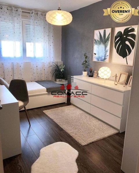 A room in a family house, wooden decor flooring, white dressers, plants, and paintings.
