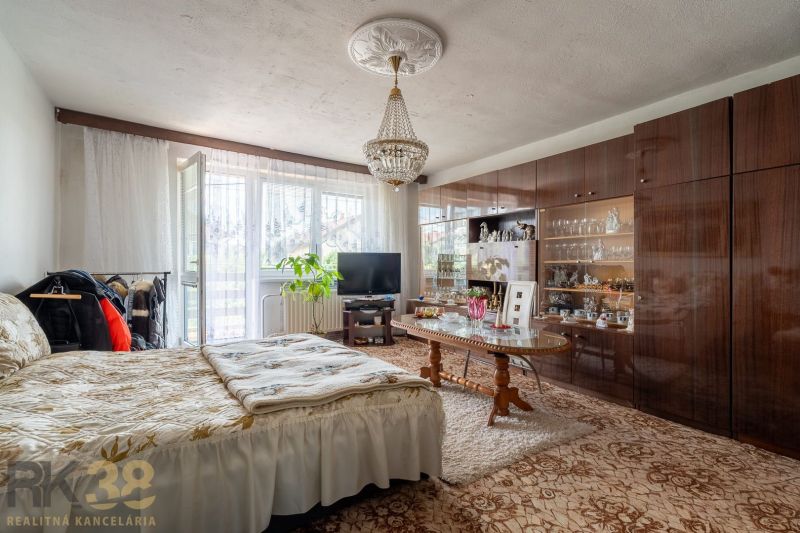 A bedroom in a family house with a bed, a living room wall unit, and a chandelier.