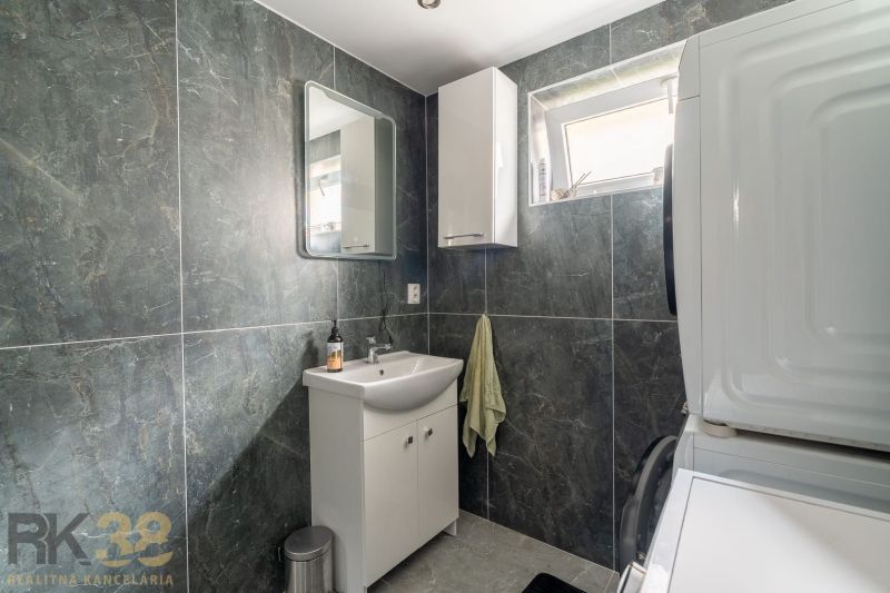 A bathroom in a family house with a sink, mirror, and appliances, surrounded by dark walls.