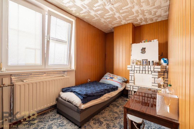 A room in a family house with a bed, a table, a radiator, and wooden paneling.