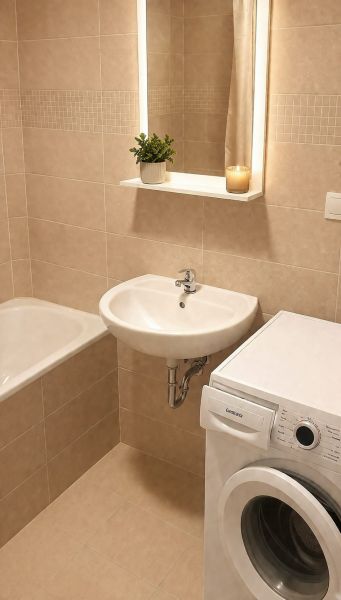Bathroom with a bathtub, sink, mirror, and washing machine in a studio apartment.