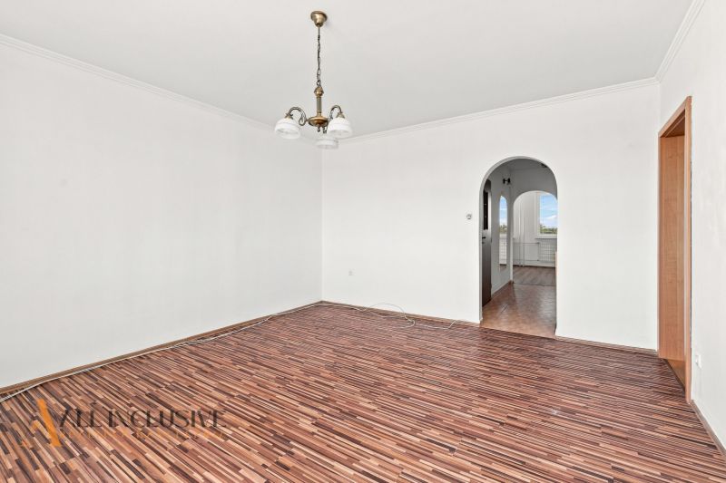 A spacious room in a 2-room apartment with a wooden decor floor and an arched passage.