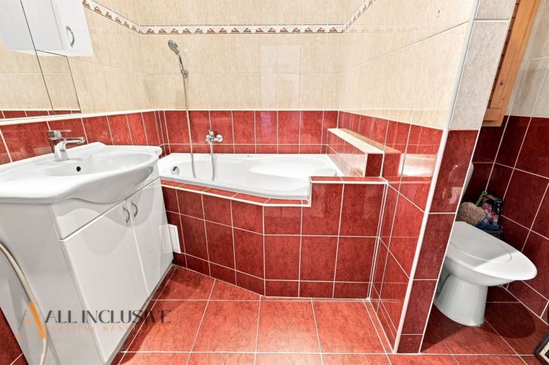 A bathroom with a bathtub and a sink in a 2-room apartment, tiled with red and beige tiles.