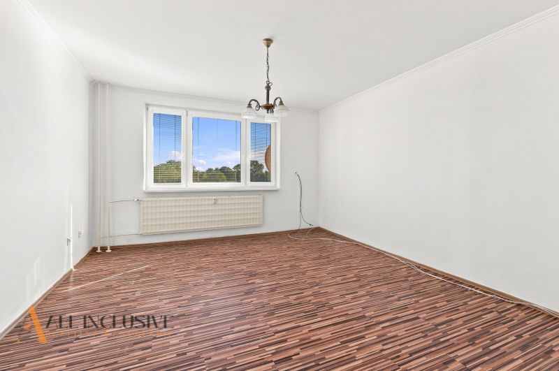 A spacious room with a wooden decor floor and a large window in a 2-room apartment.