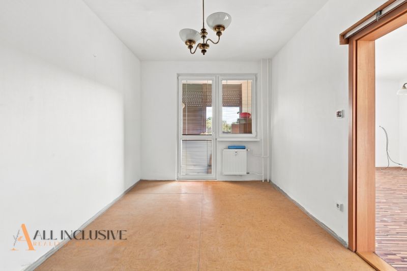 A spacious room with wooden decor, a white wall, and a light fixture in a 2-room apartment.