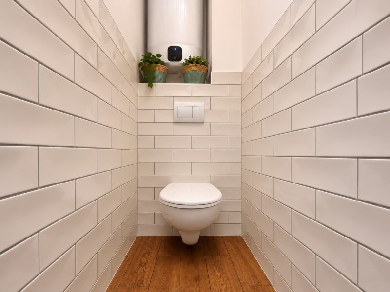 Bathroom in a 2-room apartment with white tiles and a floor with a wooden decor.