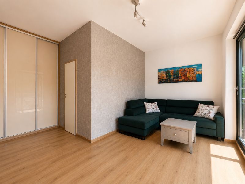 A bright living room with a corner sofa and a wooden decor floor in a 2-room apartment.