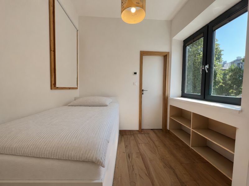 A simple room with a bed, a window, and a floor with a wooden decor in a two-room apartment.