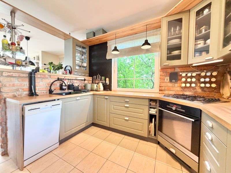 A kitchen in a family house with an oven, a counter, green cabinets, and brick tiles.
