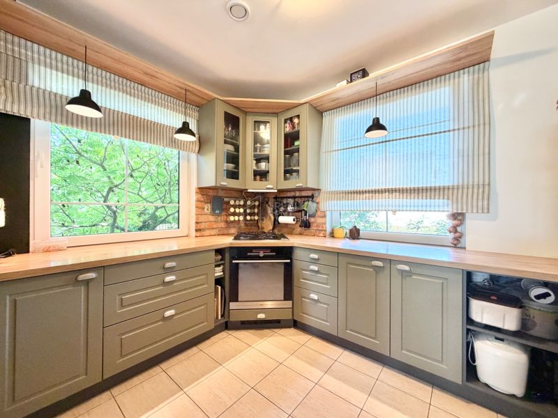 A kitchen in a family house with rustic cabinets and large windows, the lights complement the space.