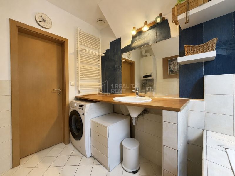 A bathroom in a family house with a washing machine, a sink, and shelves on white tiles.