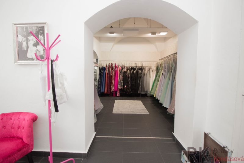 A retail space with racks full of evening dresses and a pink chair.
