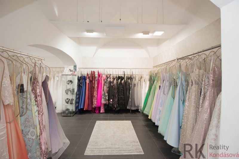 Retail space with colorful dresses, a showcase with jewelry, a carpet on a black floor.
