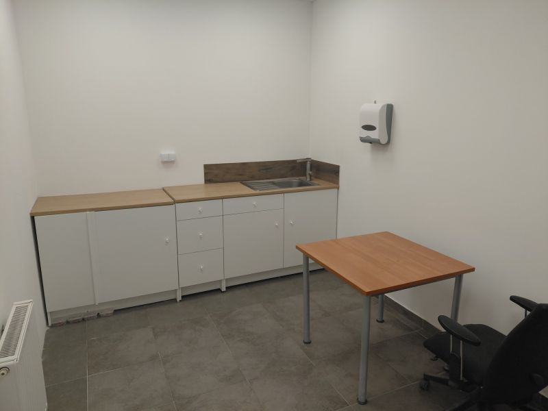Commercial space with a kitchen unit, table, and gray flooring with a wooden decor.