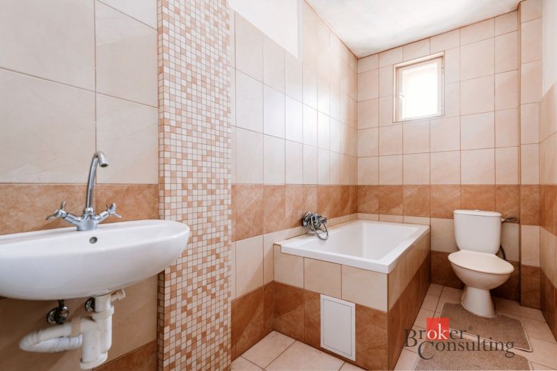 A bathroom in a family house with a bathtub, sink, and tiles in warm tones.