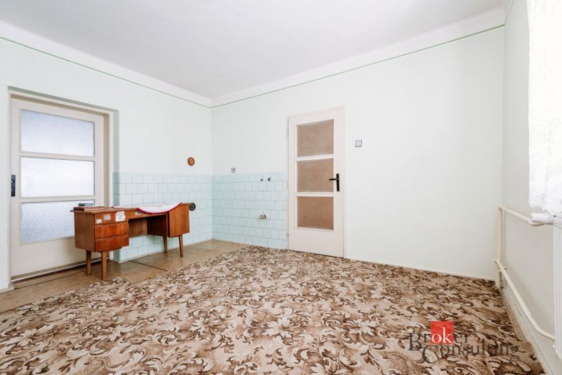 A room with a decorative carpet, a writing desk, and a tiled wall in a family house.