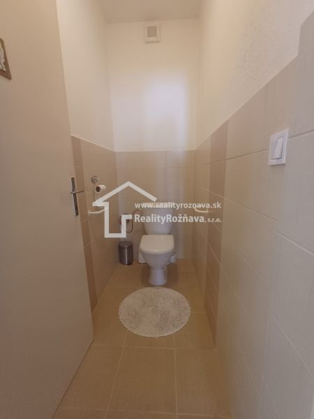 A minimalist toilet in a family house with beige tiles and a white rug.