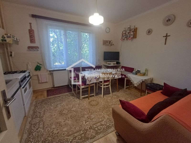 A kitchen in a family house with a gas stove, a sofa, and a television on the wall.