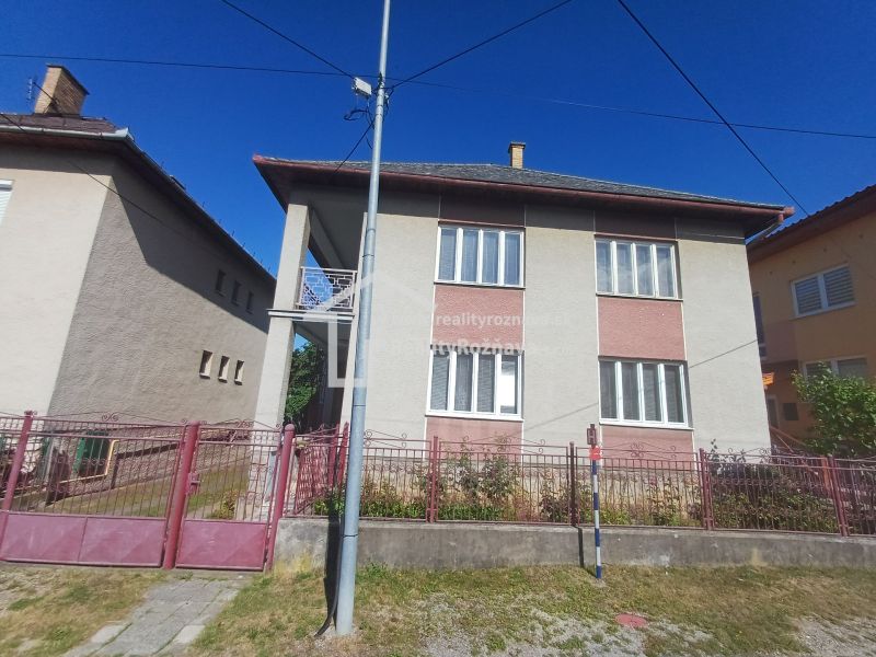 A family house in Rožňava with a brick fence, located between two other houses.