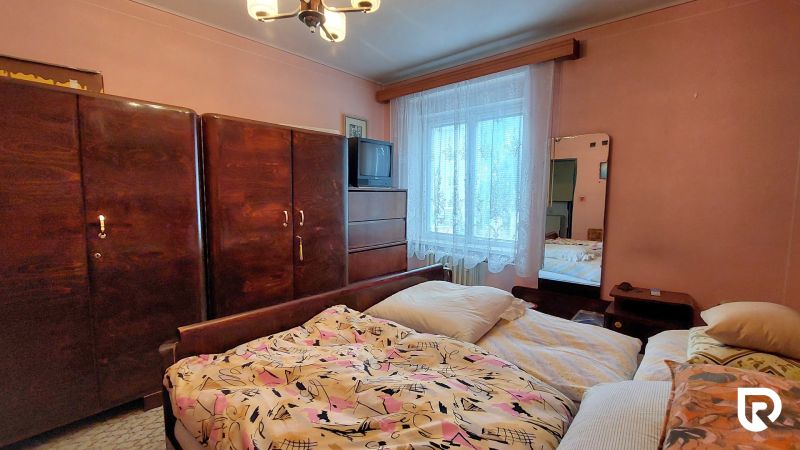 Bedroom with wooden furniture and a TV in a two-room apartment, pink walls, bed linens.