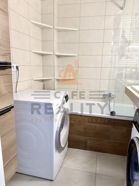 A bathroom in a 3-room apartment with a washing machine, bathtub, and shelving units.